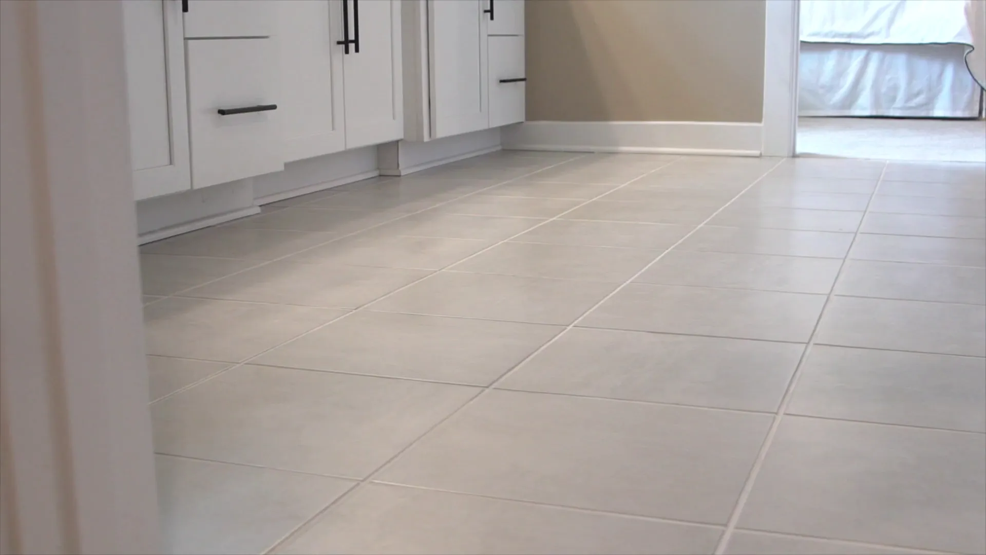 Light tile floor running past white kitchen cabinets